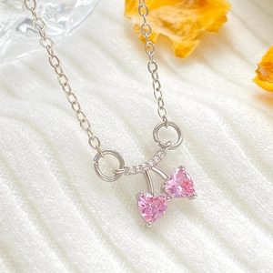Detalle del collar de corazón de cereza con circonitas rosas en tela blanca