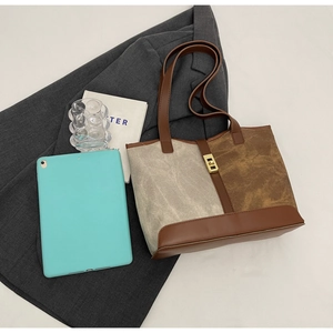Flat lay of large contrast color tote bag with golden twist lock on a grey blazer