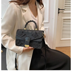 Detail of black handbag with 3D butterfly decor and twisted handle on white blazer