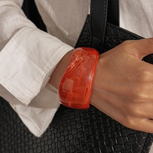 Detail of chunky orange marble acrylic bangle worn with a white linen shirt and black clutch