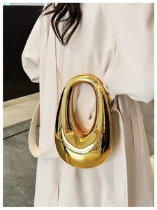 Close-up of a sculpted gold acrylic evening clutch with a hollow handle and chain strap