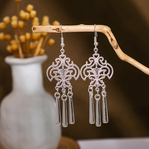 Detailed close-up of vintage silver peacock tassel earrings hanging on a dry wooden branch