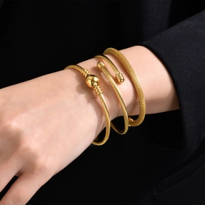 Detail of three-piece golden stainless steel bracelets with mesh and twisted textures