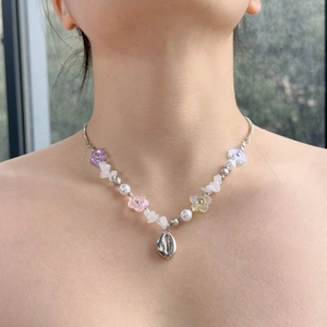 Close-up of beaded necklace with colorful flowers, white pearls, and a silver shell pendant