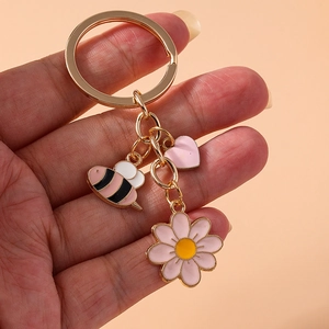Detail of pink daisy, heart, and bee charms on a gold keychain held in hand