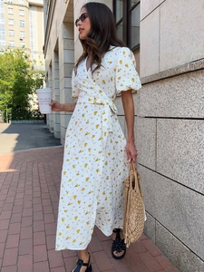 Detail of white cotton wrap dress featuring yellow floral print and tied waist ribbon