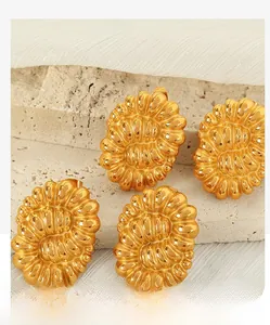 Macro shot of four gold twisted hoop earrings on textured stone and folded fabric