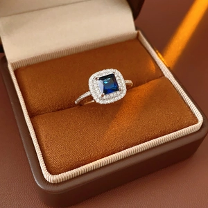 Detail of a square blue gemstone ring with double halo diamonds in a brown jewelry box