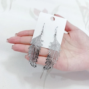Close-up of silver feather hook earrings being held for size and detail reference
