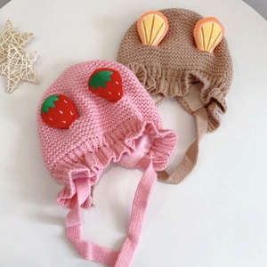 Detailed view of pink and brown knit baby hats with strawberry and orange fruit patches