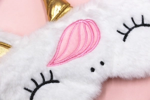 Close-up of plush unicorn sleep mask with soft white faux fur and golden horn details