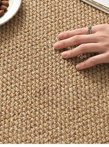 Close-up of hand touching high-density woven sisal rug with textured hazelnut fibers