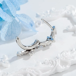 Boucle d'oreille huggie en argent avec zircons et breloque croix sur socle blanc