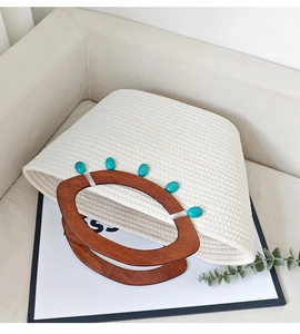 Detail of woven cream tote bag featuring dark wood handles and turquoise stone accents