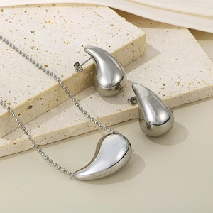 Ensemble collier et boucles d'oreilles goutte d'eau en argent sur fond pierre beige