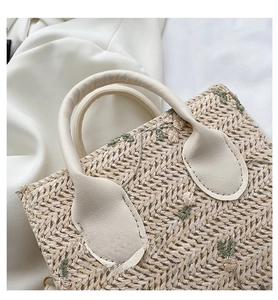 Close-up of woven straw bag with white leather handle and floral embroidery detail