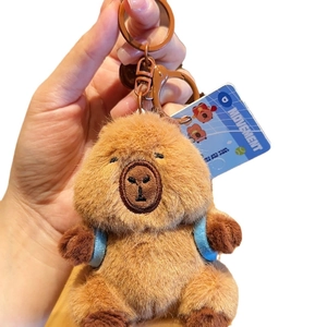 Brown plush capybara keychain with blue backpack and movement tag on white background