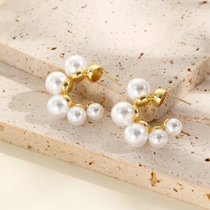Elegant U-shaped gold earrings with gradient faux pearls on a natural stone background