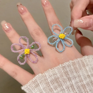 Détail de bagues fleurs artisanales en perles bleu clair et violet sur un doigt