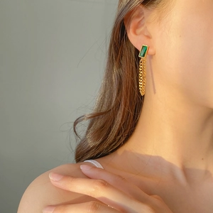 Détail de boucles d'oreilles en pierre vert émeraude avec pompons en chaîne cubaine dorée