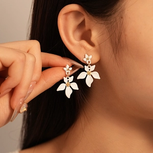 Détail de boucles d'oreilles fleurs blanches mates avec pétales superposés et étamines dorées