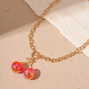 Detailed close-up of cherry pendant necklace with gold chain and green leaf on stone