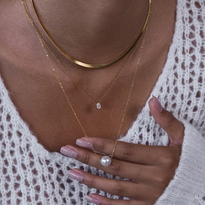 Détail d'un collier doré à plusieurs rangs avec zircon goutte et pendentif perle