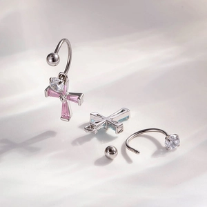 Silver curved barbell piercing set with pink and blue zircon cross charms on beige fabric