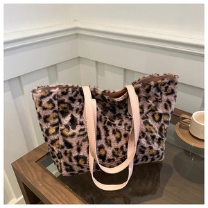 Détail du sac cabas en peluche léopard avec des poignées en cuir rose sur table en bois