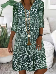 Detailed close-up of a green floral V-neck dress with a long wooden bead necklace and tassel