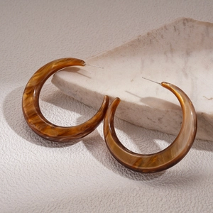 Detailed view of large C-shaped amber resin earrings against a textured marble stone