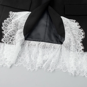 Detailed close-up of intricate white eyelash lace hem on a black tailored blazer jacket