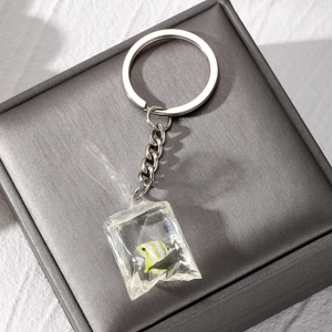 Detailed close-up of a resin water bag fish pendant keychain on a grey jewelry box cover