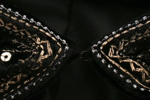 Détail de broderie sur velours noir avec paillettes dorées et fermeture en métal