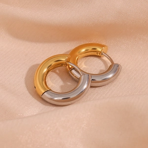 Detail of two-tone gold and silver C-shaped hoop earrings on champagne silk fabric