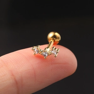 Macro shot of a gold tragus stud with three white zircons held between fingertips