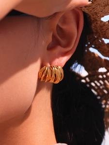Detailed view of gold multi-layered C-shaped earrings worn on an ear in sunlight
