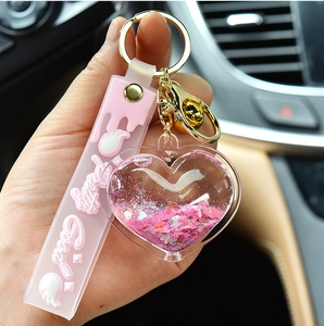 Detail view of pink heart quicksand keychain with glitters, bell and silicone strap.