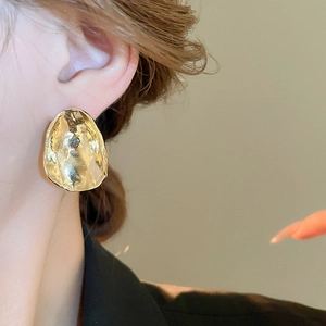 Close-up of golden irregular wavy metal earrings on model showing mirror texture