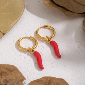 Detailed close-up of golden hoop earrings with red enamel chili pepper charms on white texture
