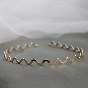 Dettaglio di un elegante cerchietto metallico dorato ondulato su pietra grigia