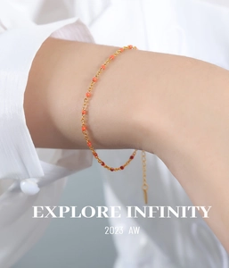 Detail of gold chain bracelet with red enamel beads worn on wrist over a white shirt