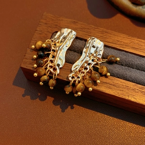 Dettaglio di orecchini vintage dorati con texture a onde e perle pendenti di occhio di tigre