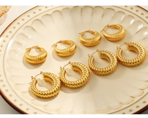 Dettaglio orecchini placcati oro con texture a croissant su piatto di porcellana vintage