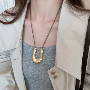 Dettaglio di una collana con pendente a U dorato indossata su un trench beige