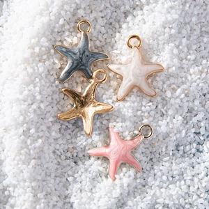 Mini colorful alloy starfish pendants in four colors displayed on a white sand background