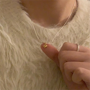 Close-up of a minimalist golden heart pendant necklace worn on a soft beige knit sweater