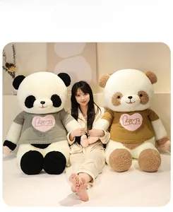 Close-up of large plush panda toy wearing a knitted heart sweater in a bedroom setting