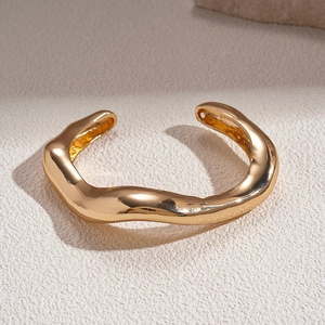 Detail view of the polished golden irregular wave texture on the open bangle bracelet