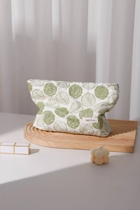 Close-up of white cotton linen cosmetic bag with green leaf embroidery on wooden tray